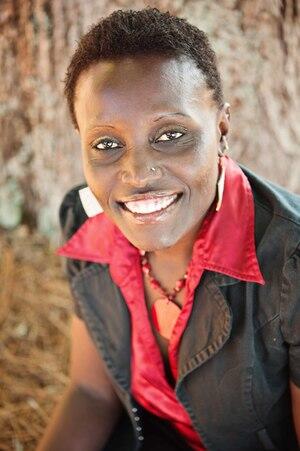 Dr. Ngumbi smiling in a red button up shirt with a black blazer jacket over it.